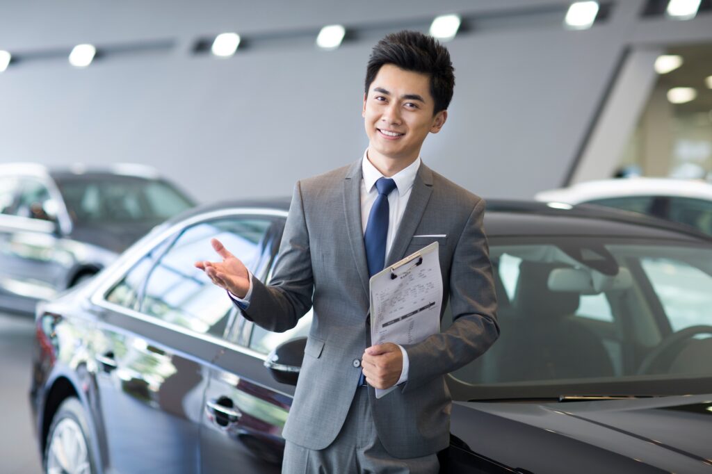 Confident salesman standing with new cars in showroom